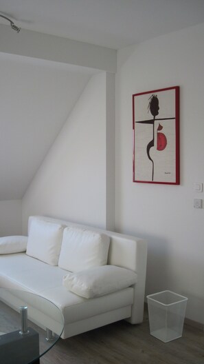 Un canapé blanc dans une pièce dotée d’un plafond en pente et d’une œuvre d’art abstraite encadrée accrochée au mur.
