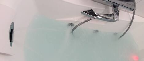 A modern bathroom with a chrome faucet, a visible drain, and a clear view of the water in the tub.
