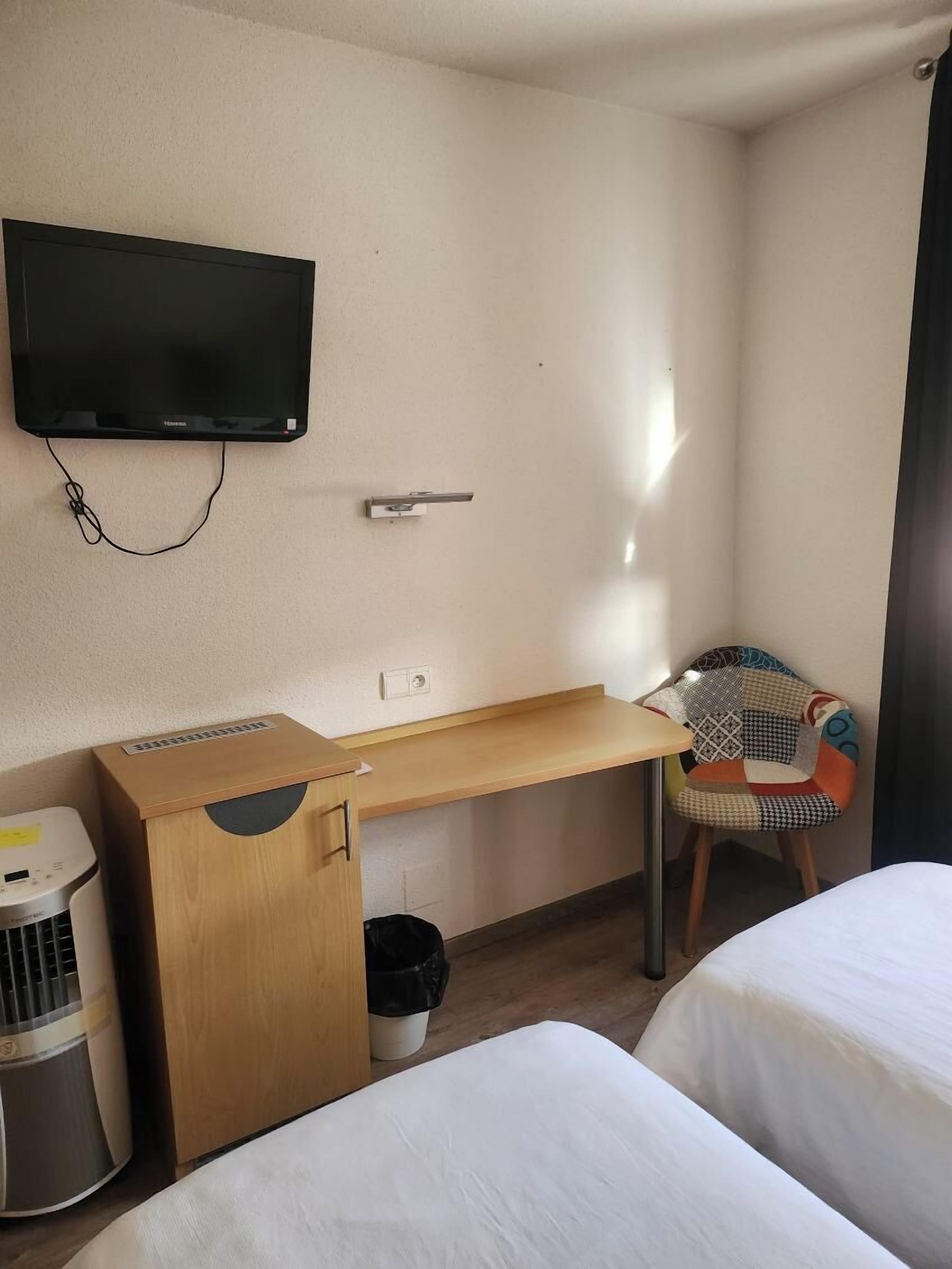 Ein Hotelzimmer mit Holztisch, Wandfernseher, Stuhl und zwei Betten.