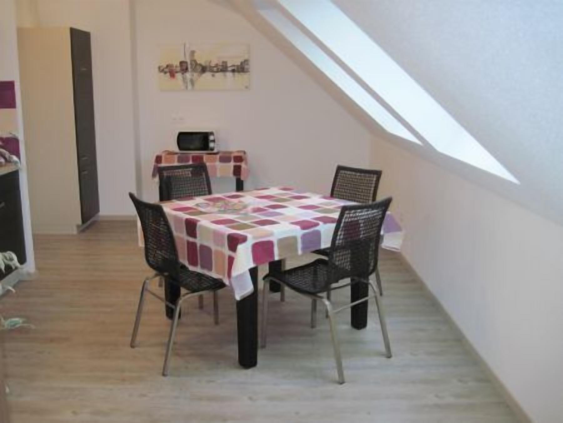 Un comedor con una mesa cubierta por un mantel a cuadros, cuatro sillas y un cuadro en la pared.