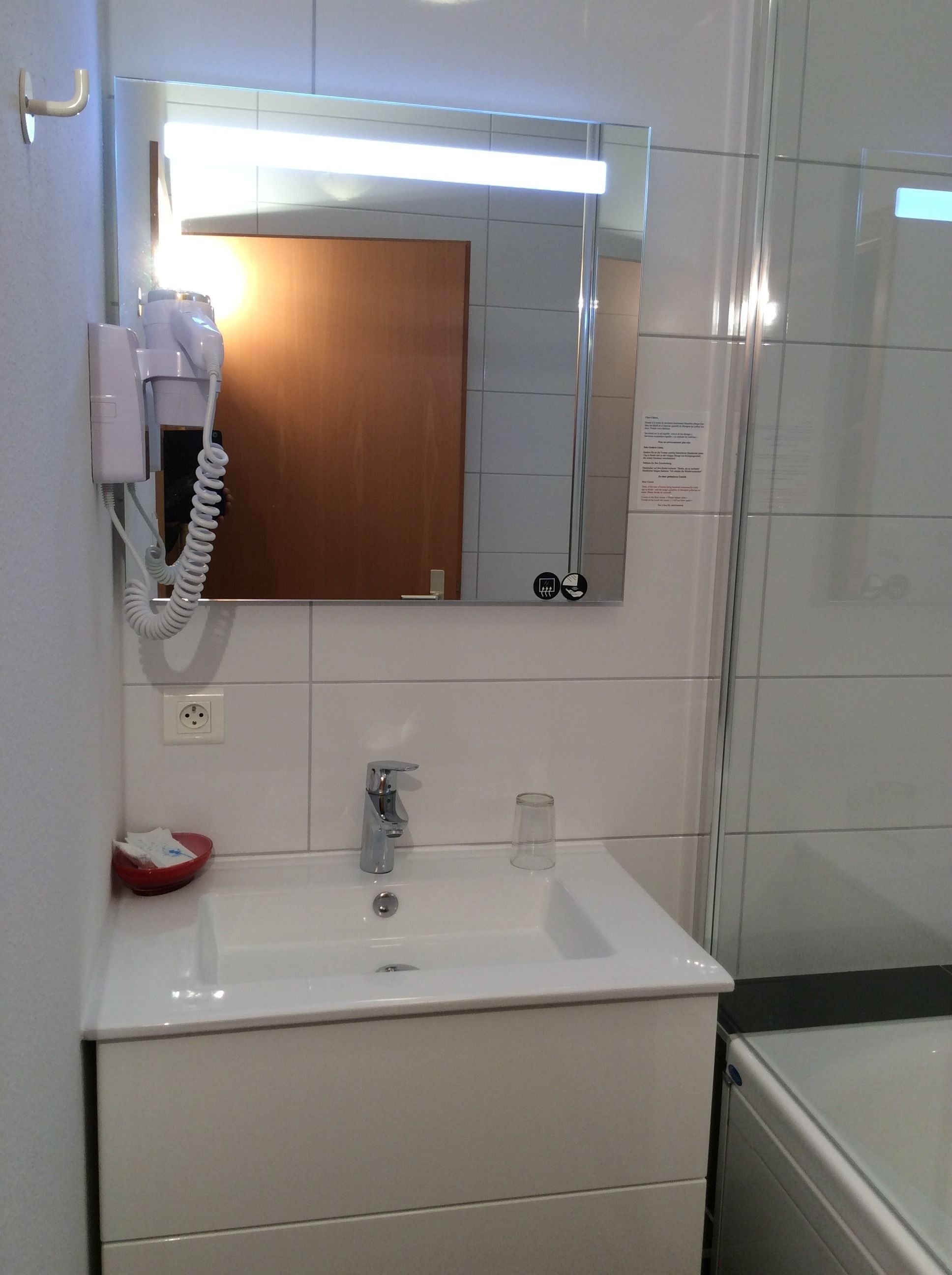 Ein Badezimmer mit einem weißen Waschbecken, einem Spiegel, einem Haartrockner und einer roten Schüssel.