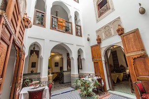 Pátio interior com arcos, área de refeições e vista para um quarto com mesa e cadeiras.