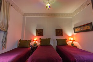 Quarto com duas camas, cada uma com colcha vermelha e travesseiro verde, e duas luminárias fixadas na parede.