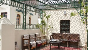 A covered outdoor seating area with a patterned rug, wooden furniture, and a decorative metal fence. - Dar Fes Medina Ziat (Fes)