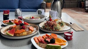 Un espace de restauration aménagé sur le toit, offrant une vue sur le paysage urbain, avec une table dressée avec différents plats, une cafetière et un canapé.