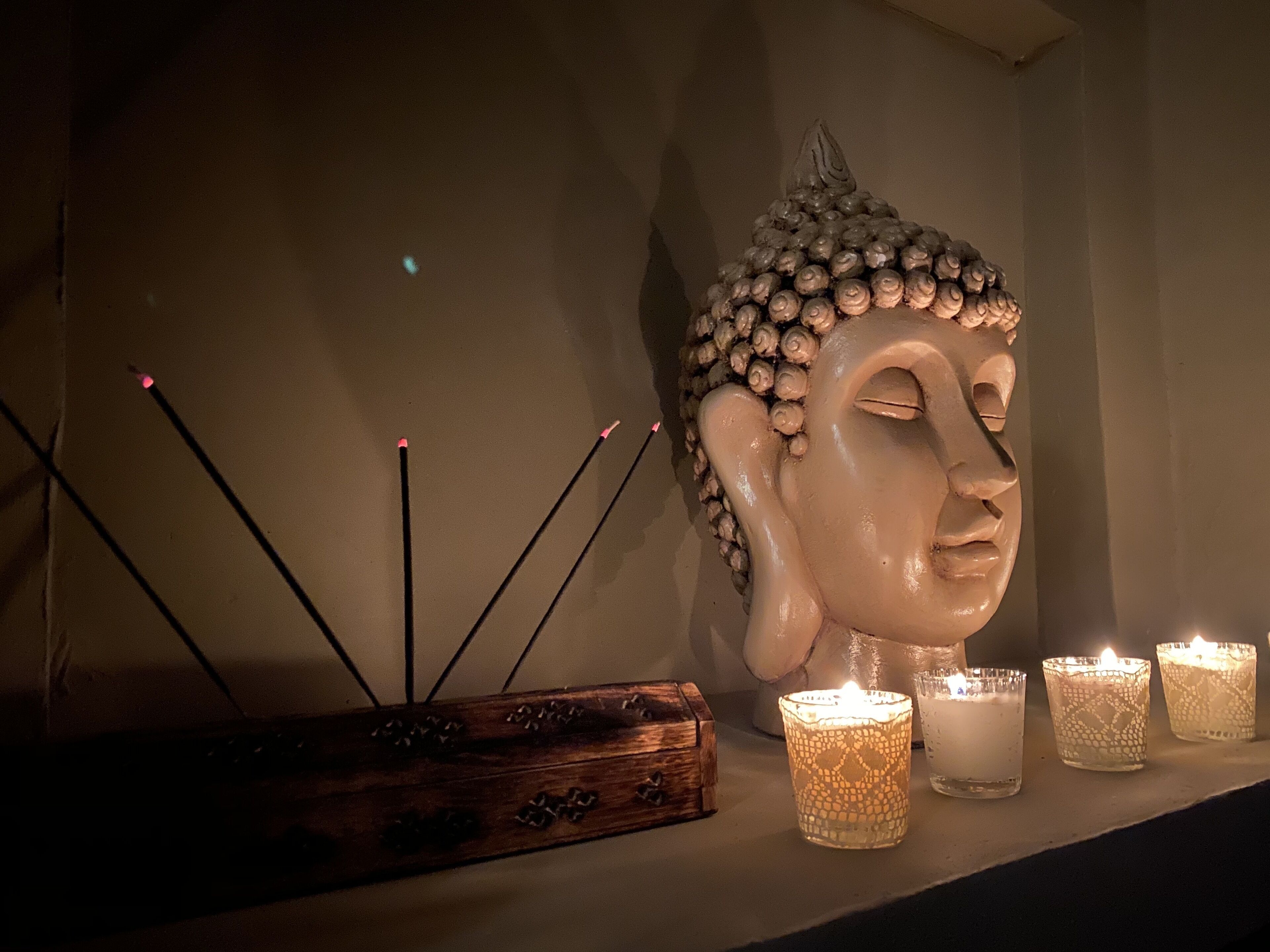 Una escultura de cabeza de Buda, palitos de incienso y tres velas encendidas sobre una estantería.