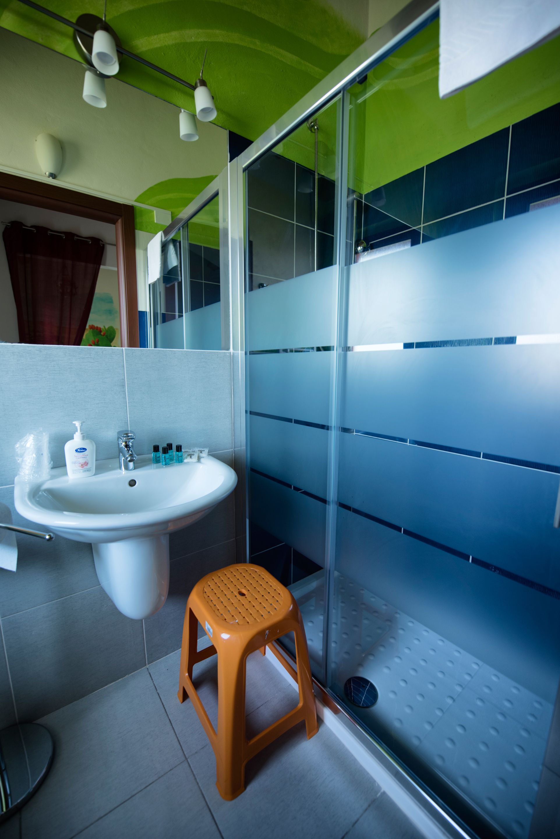 A bathroom with a white sink, a wooden stool, and a glass shower enclosure.