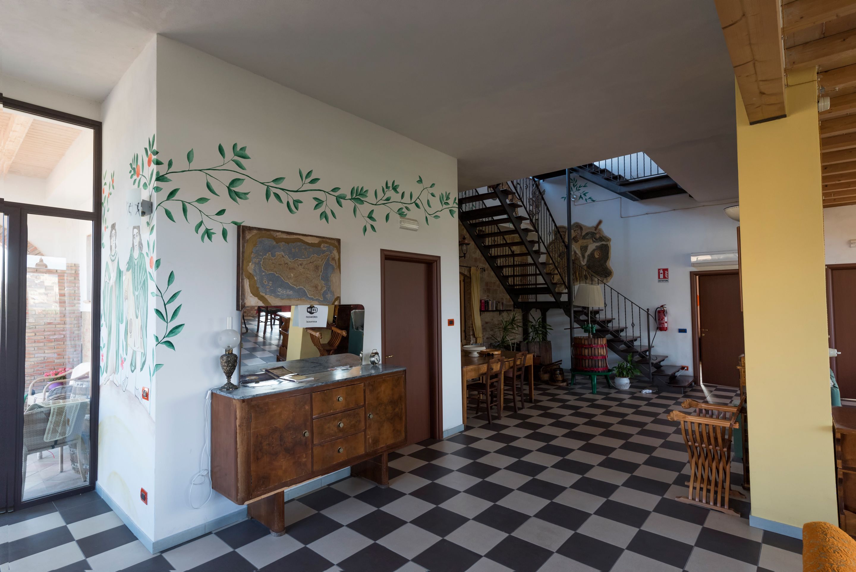 Un vestíbulo amplio con piso a cuadros, un mostrador de recepción de madera, una escalera y un gran mapa en la pared.