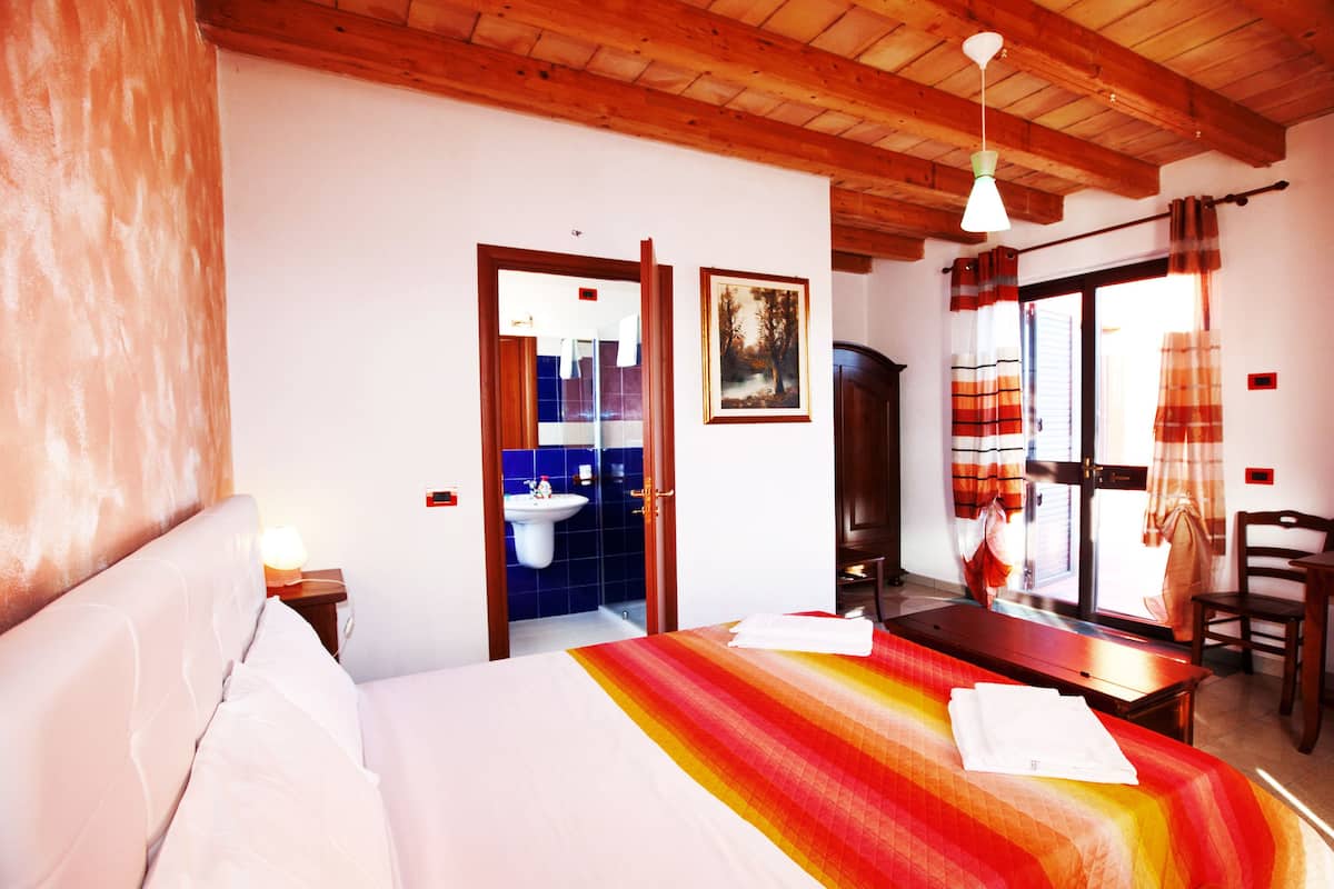 Ein Hotelzimmer mit Bett, Schreibtisch, Stuhl, einem Fenster mit Vorhängen, einem Waschbecken und einer Tür zu einem Badezimmer.