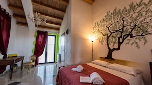 A hotel room with a bed, a desk, a chair, a chandelier, and a wall mural. - La Casa Rossa Country House (Piazza Armerina)
