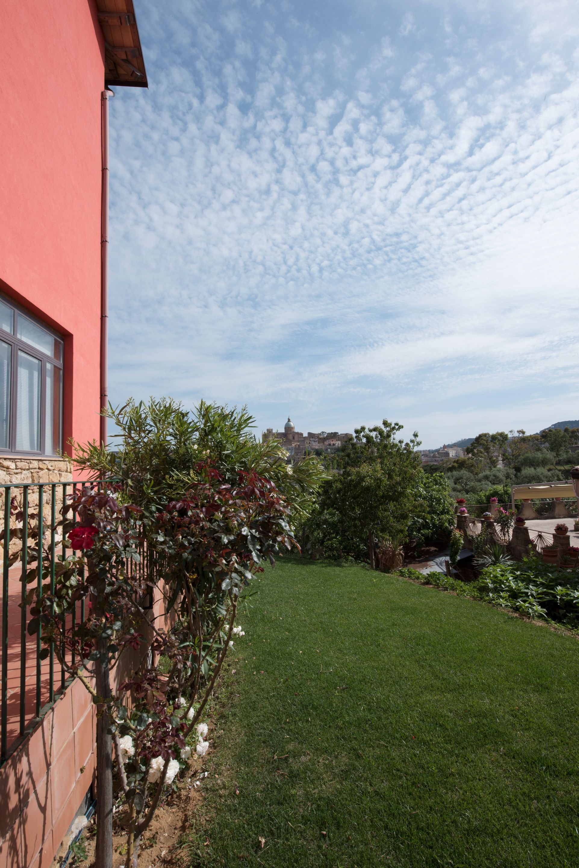 A red building with a fenced garden, a clear sky, and distant hills.