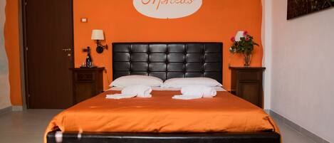 A hotel room with an orange wall, a black headboard, and a bed with white linens.