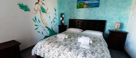 A bedroom with a bed, a nightstand, a dresser, a wall mural, and a painting.