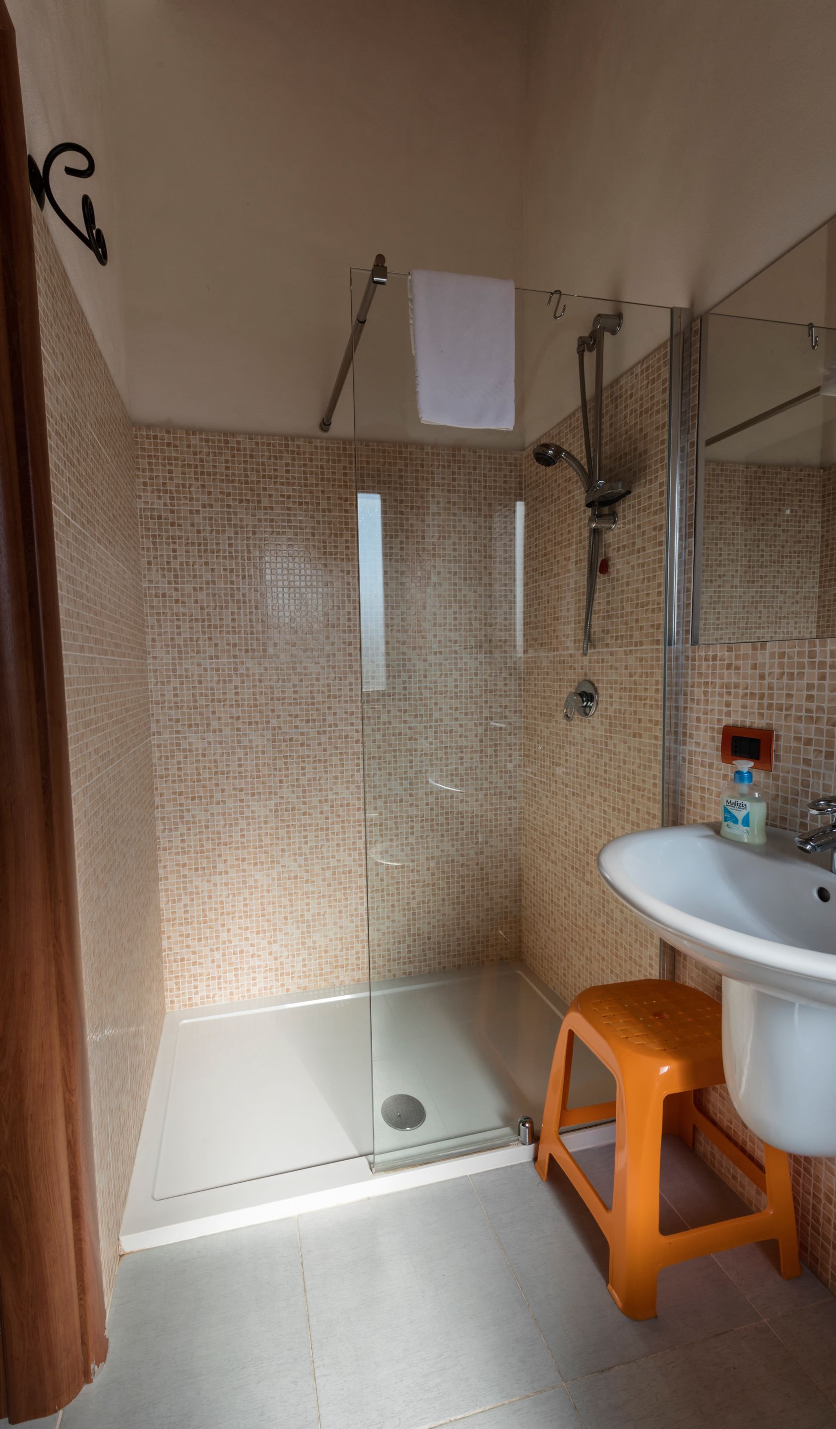 A bathroom with a glass-enclosed shower, a white sink, and a small orange stool.