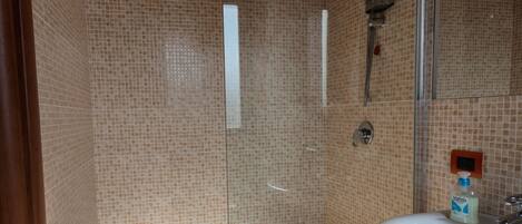 A bathroom with a glass-enclosed shower, a white sink, and a small orange stool.