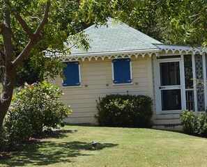 A single-story house with a gabled roof, a front porch with a white railing, and a small front yard with a tree and shrubs. - Dolphin House Villa (Newcastle)
