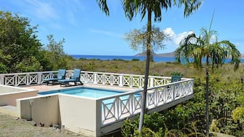 A pool area with a white fence, lounge chairs, and a view of the ocean.