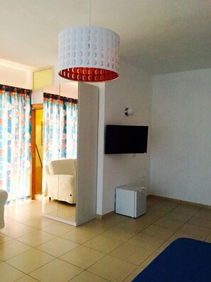 Una habitación de hotel moderna con una cama grande, un televisor de pantalla plana en la pared y un pequeño armario blanco.