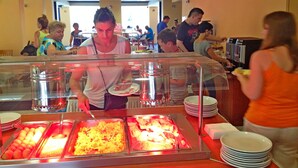 Zona de bufé con varias estaciones de comida, incluyendo una de alimentos calientes y una presentación de frutas frescas.