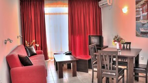 A living room with a red sofa, a TV, a dining table with chairs, and a painting on the wall. - Hotel Andromeda - All inclusive (Sunny Beach)