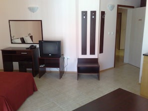 A hotel room with a bed, a desk with a television, a mirror, and a door with a number.