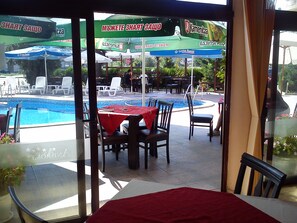 Restaurante junto a la piscina con mesas al aire libre, piscina y sombrillas.