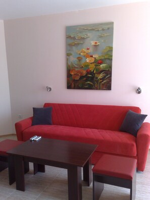 A living room with a red sofa, two dark wooden tables, and a painting of flowers on the wall.