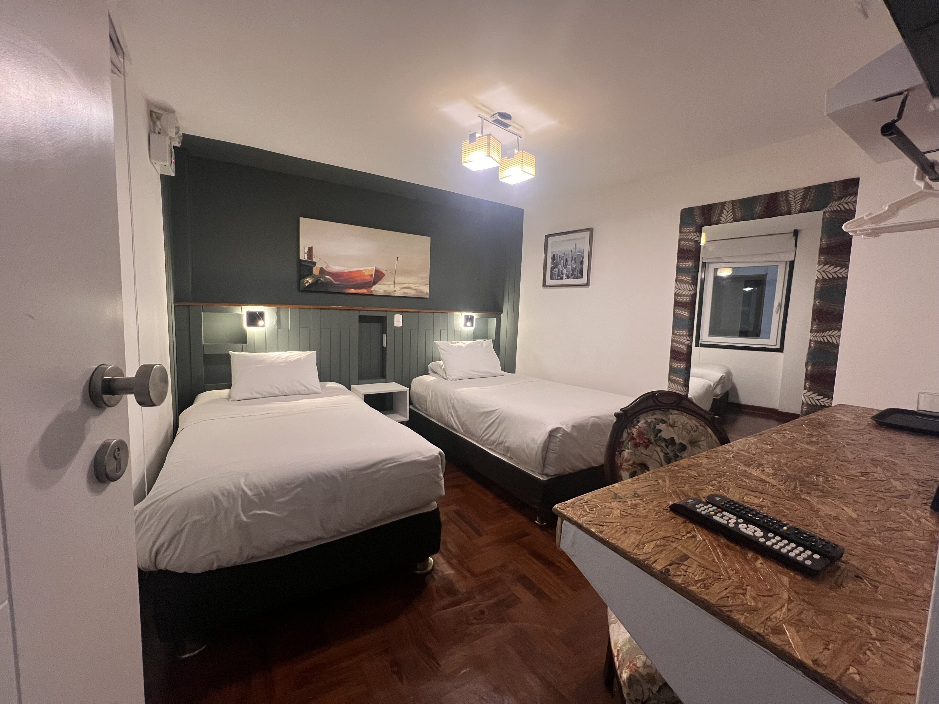 Habitación de hotel con dos camas, piso de madera, un cuadro en la pared, una ventana con vistas y un control remoto sobre el mostrador.