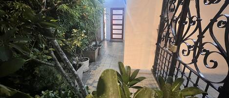 Un estrecho sendero bordeado por macetas con plantas que conduce a una puerta con un portón de metal.