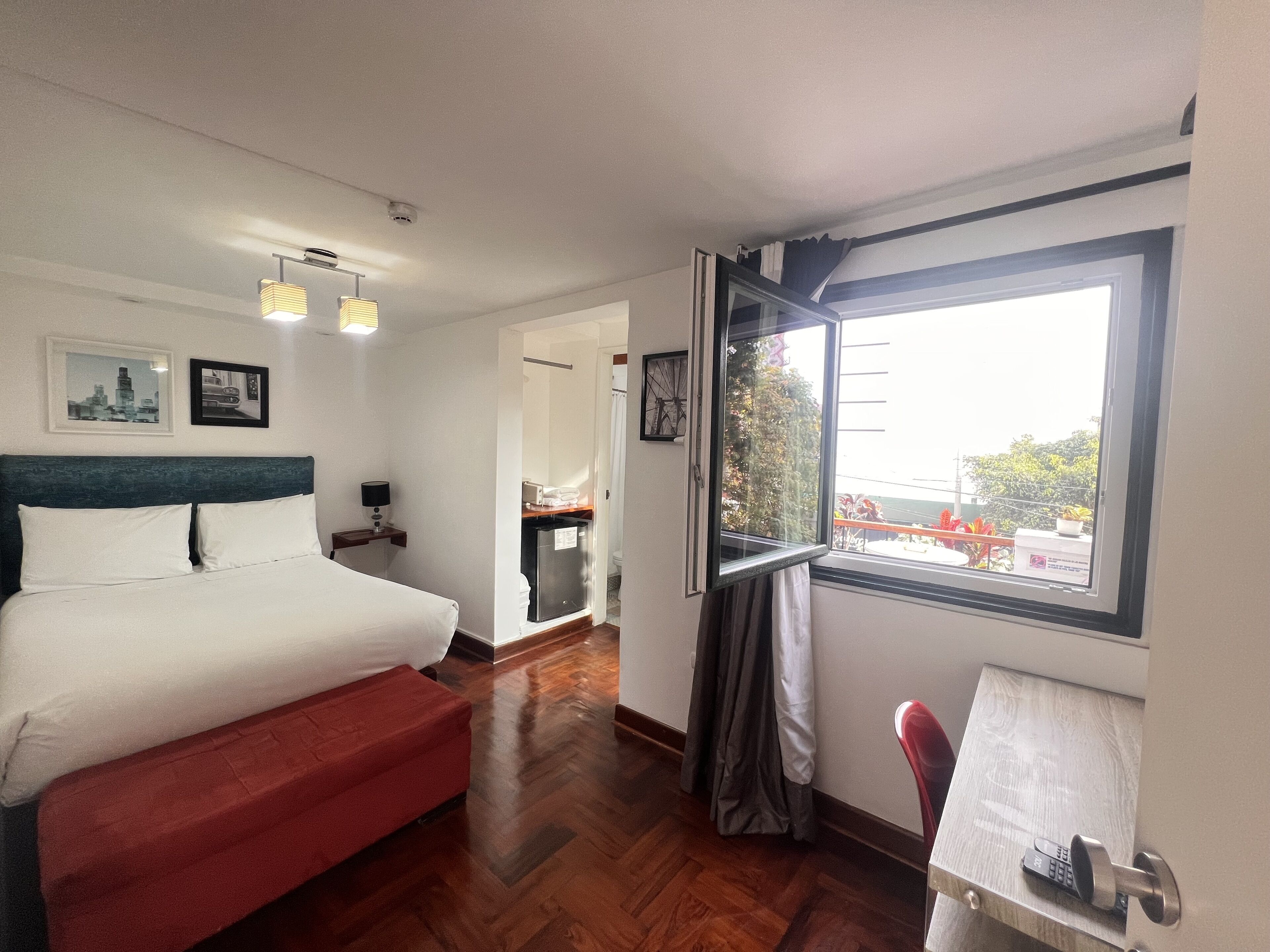Habitación de hotel con cama, escritorio, ventana con vistas al exterior y puerta que da a otra habitación.