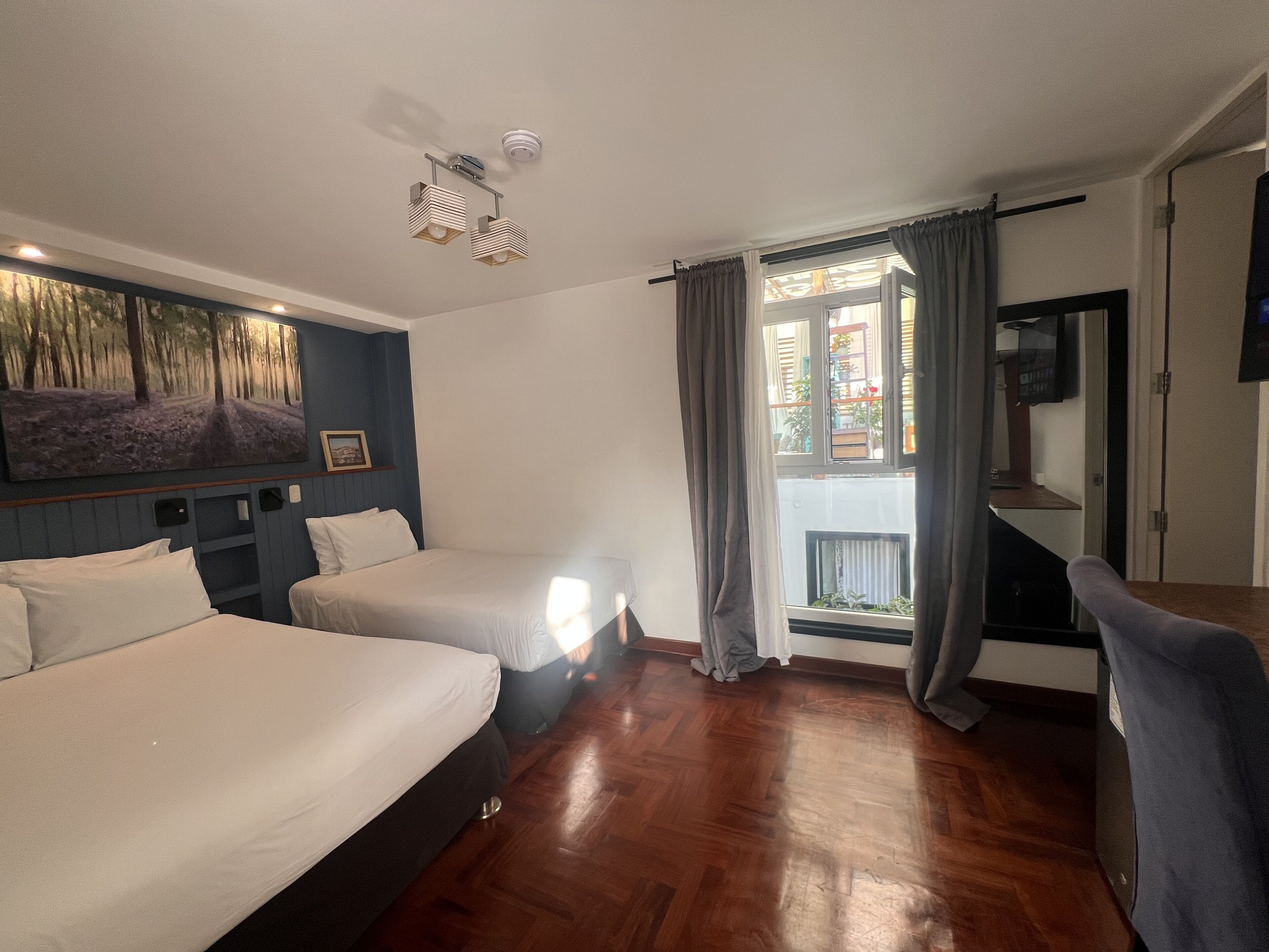 A hotel room with two beds, a painting on the wall, a desk with a chair, and a window with curtains.