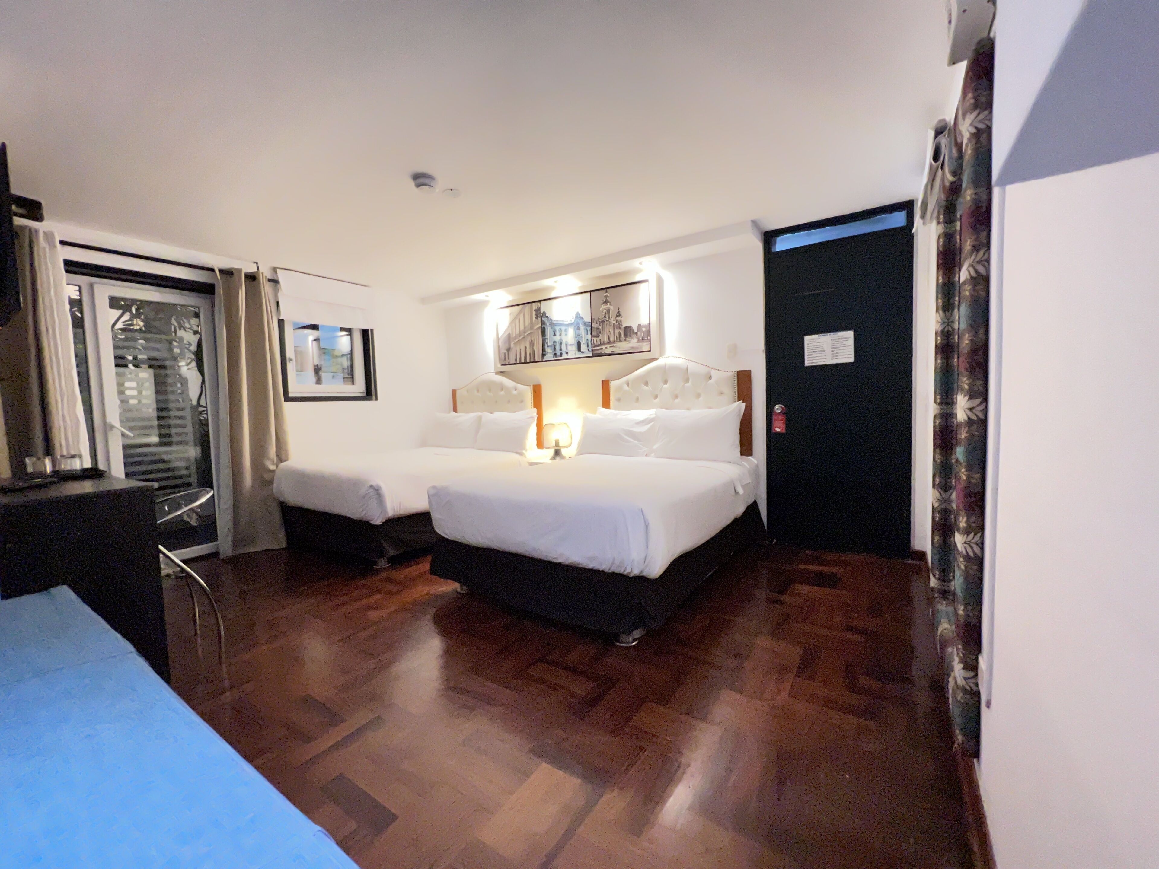 A hotel room with two beds, a desk, a chair, and a window with blinds.