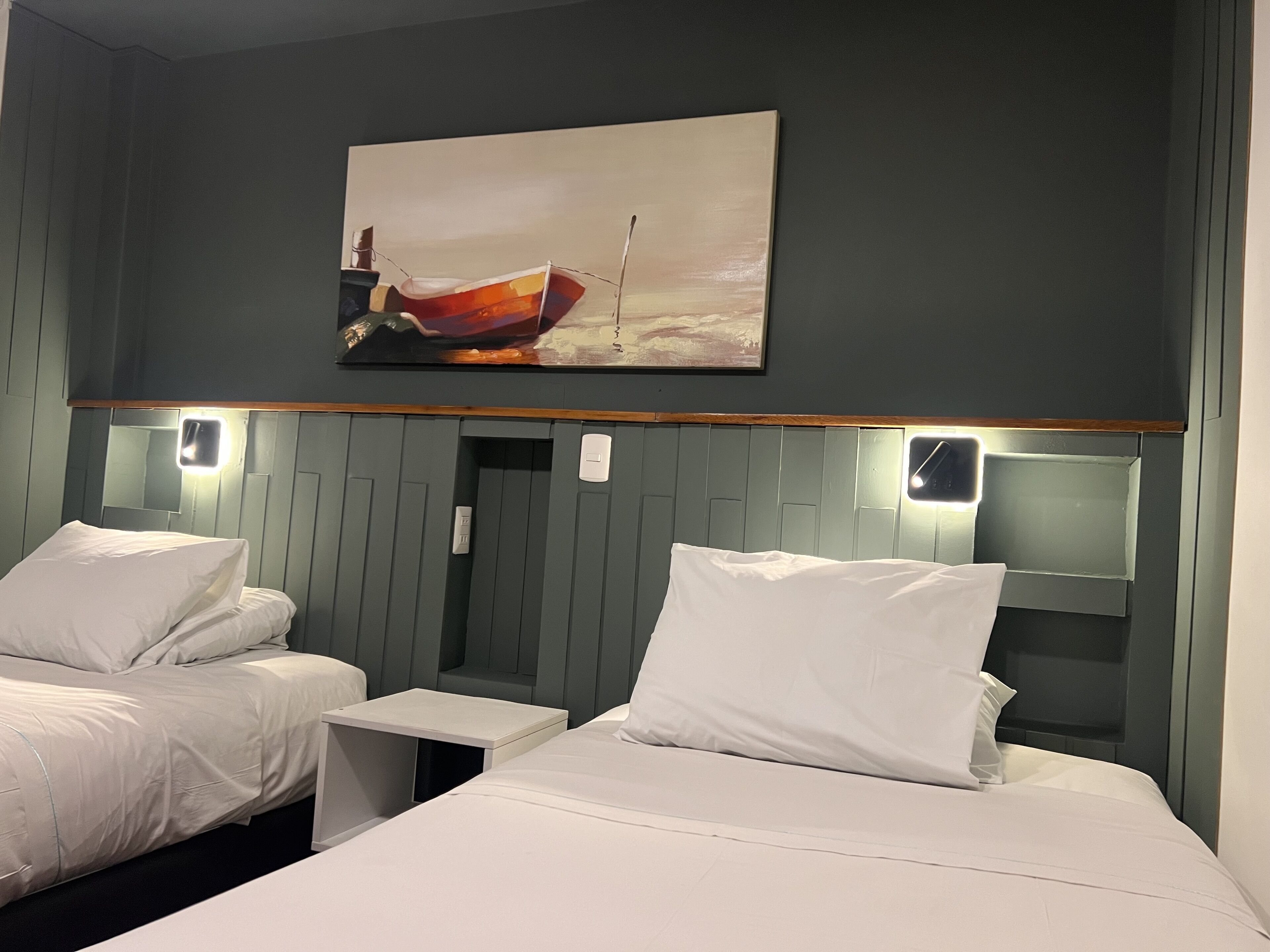 A hotel room with two beds, a painting of a boat on the wall, and bedside lamps.