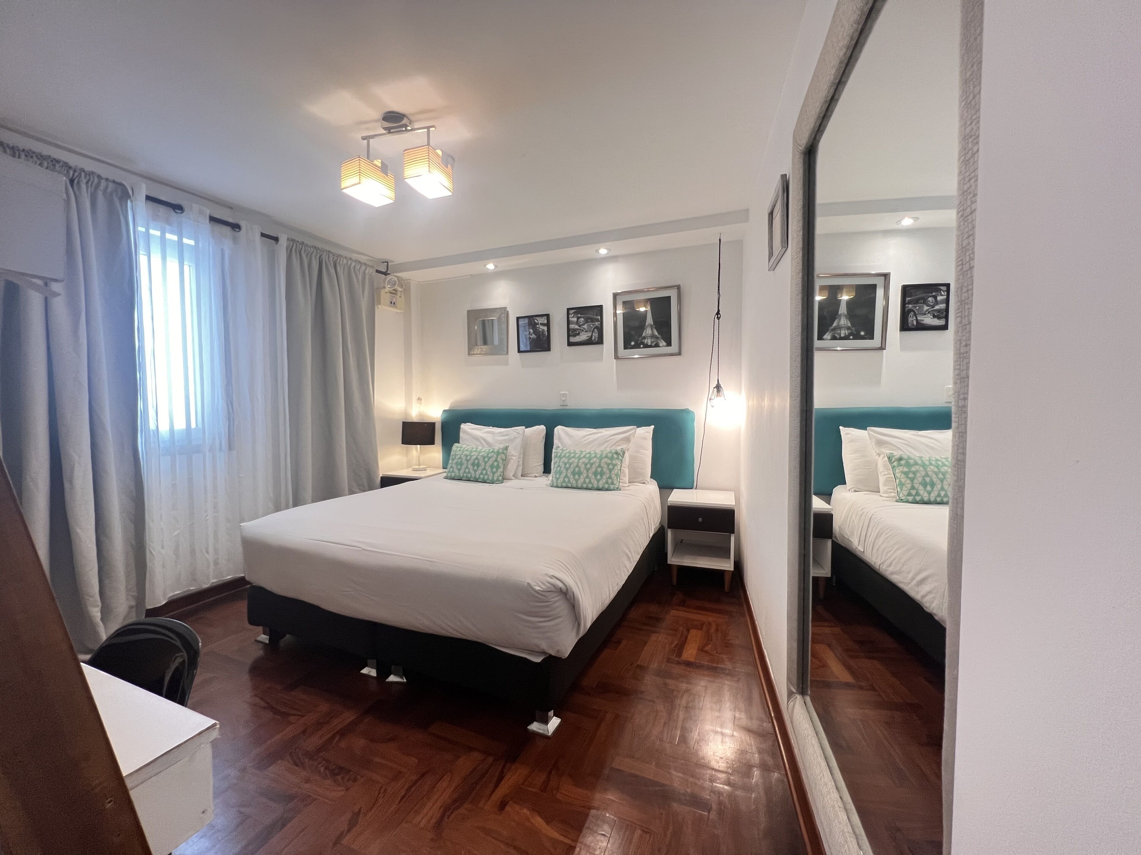 A hotel room with a large bed, bedside tables, a mirror, and wall-mounted pictures.