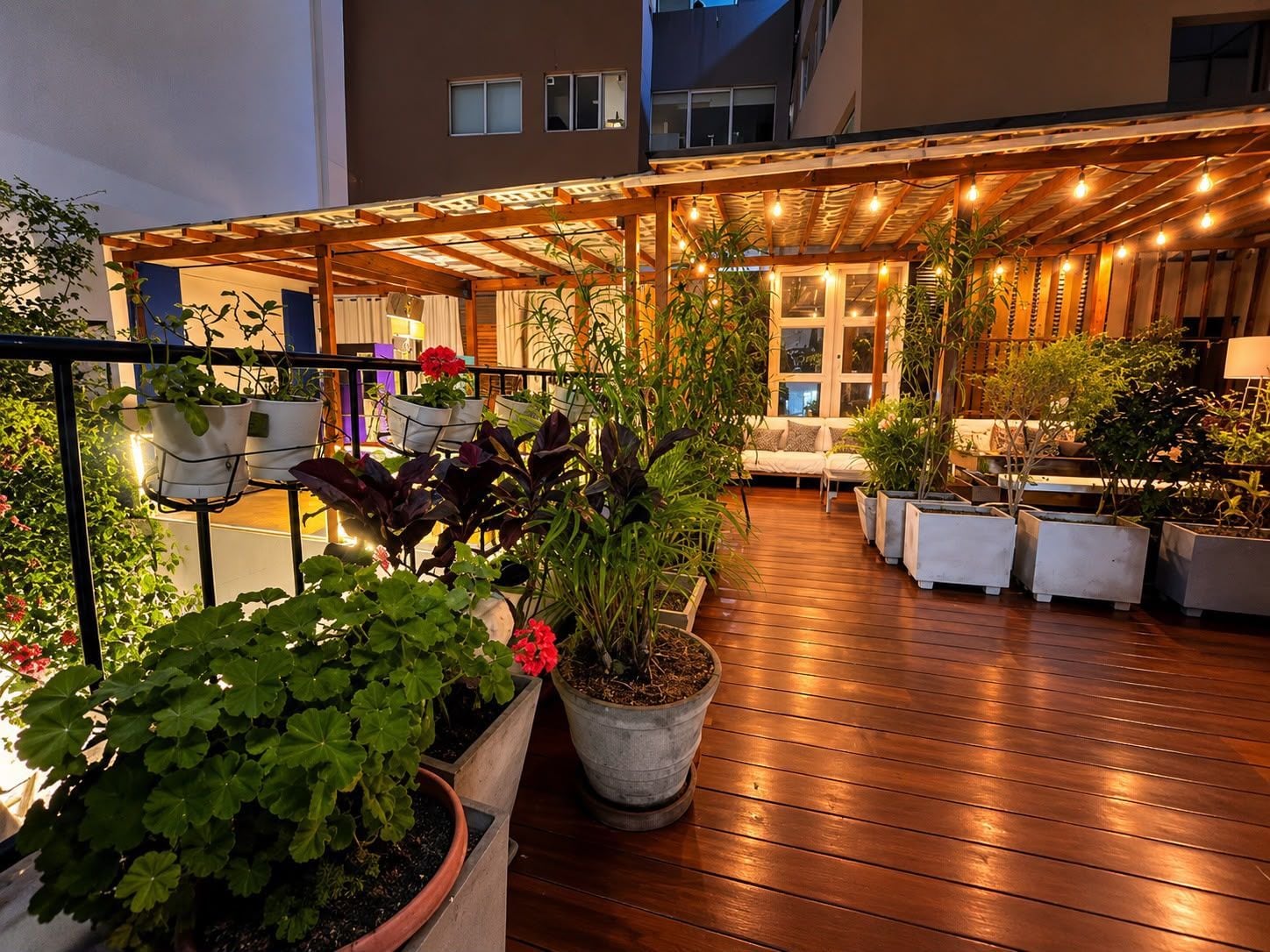 An outdoor patio area with wooden flooring, potted plants, and a seating arrangement.