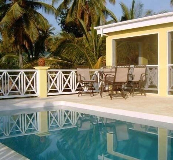A poolside area with a table and chairs, surrounded by a white fence and palm trees. - Yellow Bird Villa (Barnes Ghaut)