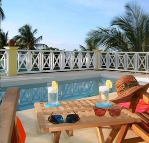 A poolside area with a table, two glasses of water with lemon slices, sunglasses, and a straw hat. - Yellow Bird Villa (Barnes Ghaut)