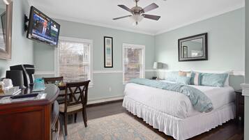 A bedroom with a bed, a desk, a chair, a television, and a ceiling fan.