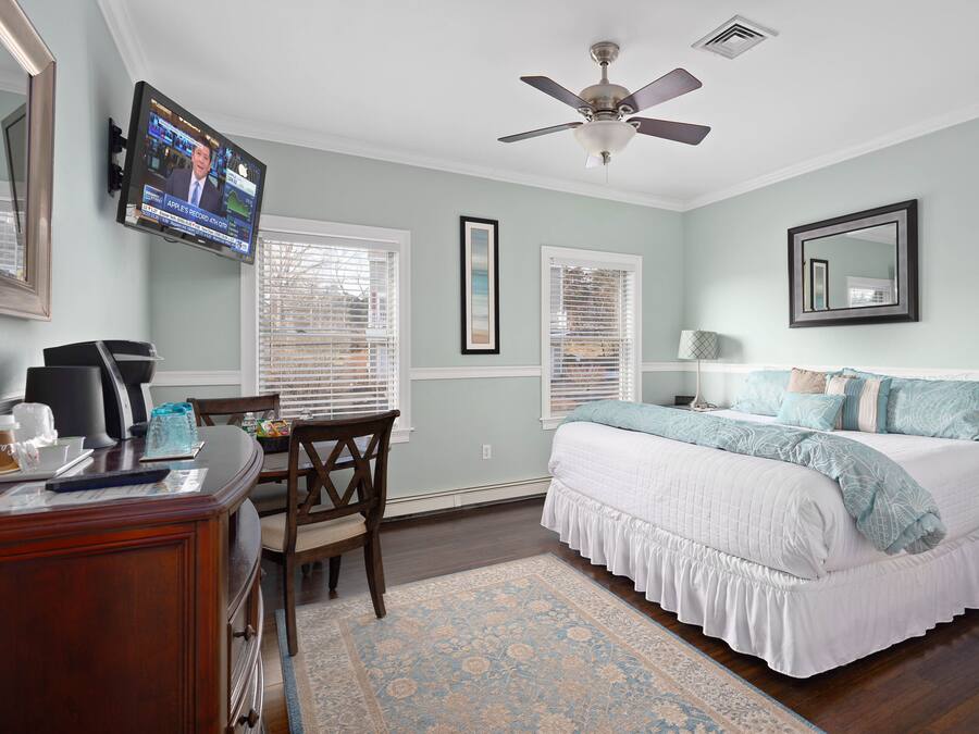 A bedroom with a bed, a desk, a chair, a television, and a ceiling fan.