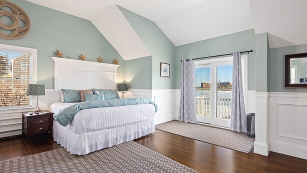 A bedroom with a large bed, a nightstand, a window with blinds, a balcony with a view, and a ceiling with a skylight. - The Beacon Waterfront Inn (Hull)