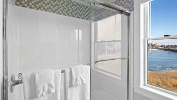 Un baño moderno con cabina de ducha de vidrio, azulejos blancos y vistas a un paisaje urbano a través de un ventanal grande.