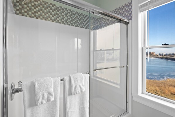 A modern bathroom with a glass shower enclosure, white tiles, and a view of a cityscape through a large window. - The Beacon Waterfront Inn (Hull)