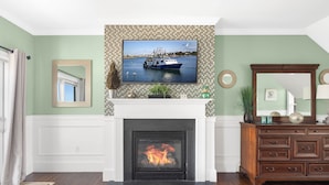 A living room with a fireplace, a television mounted above it, and a wooden dresser to the right. - The Beacon Waterfront Inn (Hull)