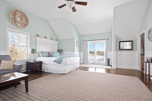 A spacious bedroom with a large bed, a ceiling fan, and a view through a sliding glass door.