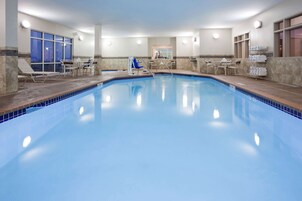 Una piscina interior con agua cristalina y azul, rodeada de sillas y tumbonas.