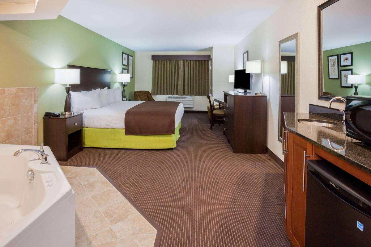 A hotel room with a bed, a desk, a chair, a television, a sink, and a mirror.