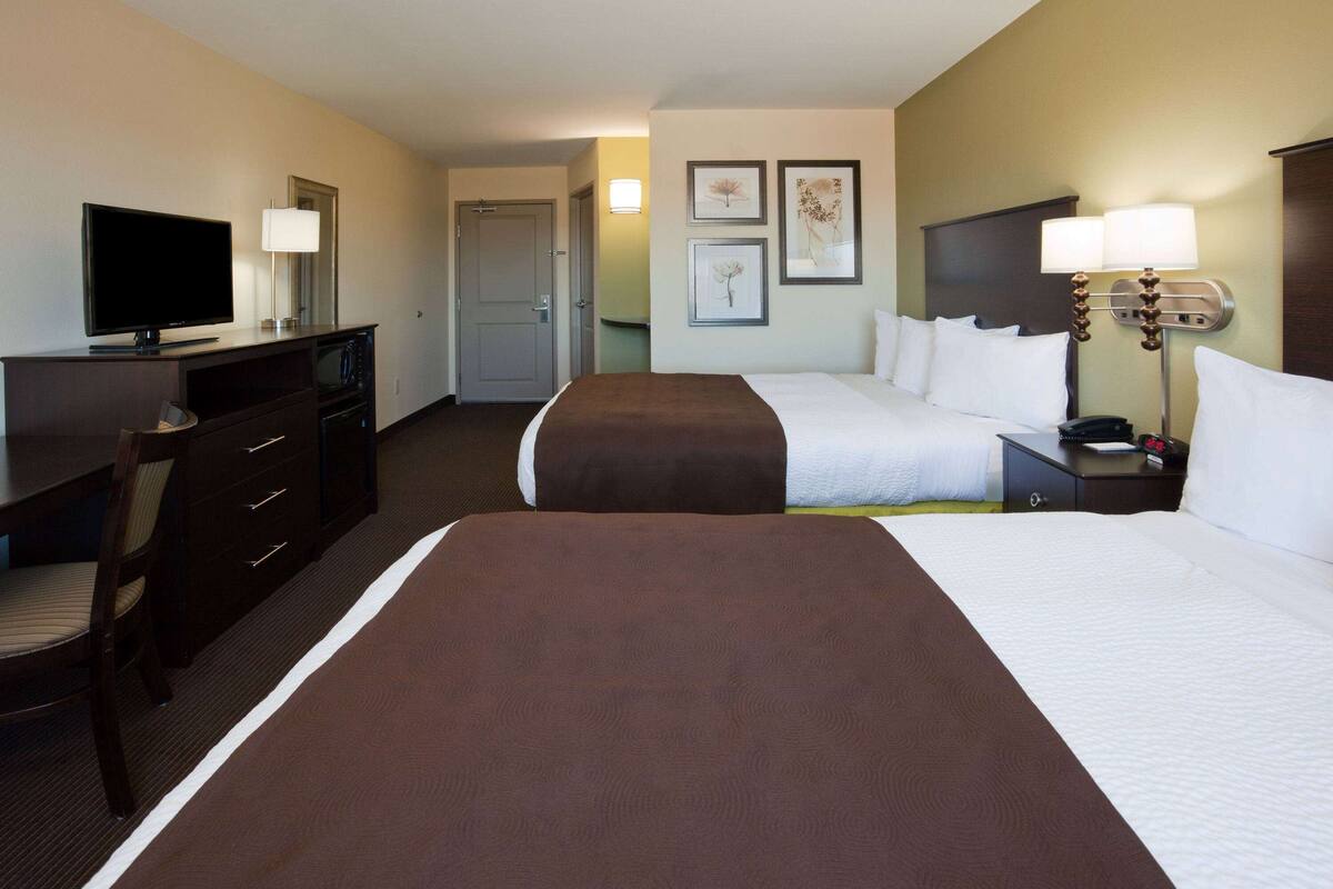 A hotel room with two beds, a TV, a desk, and a chair.