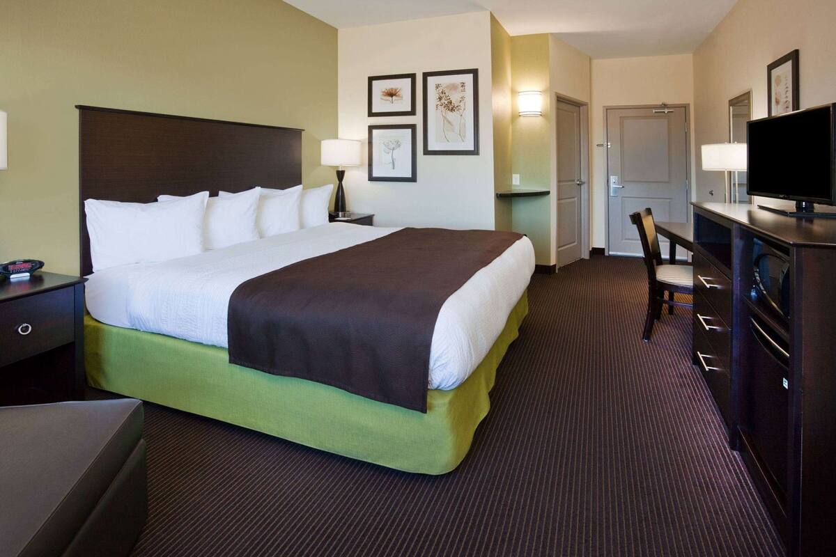 A hotel room with a large bed, bedside tables, a desk with a chair, a television, and framed artwork on the wall.