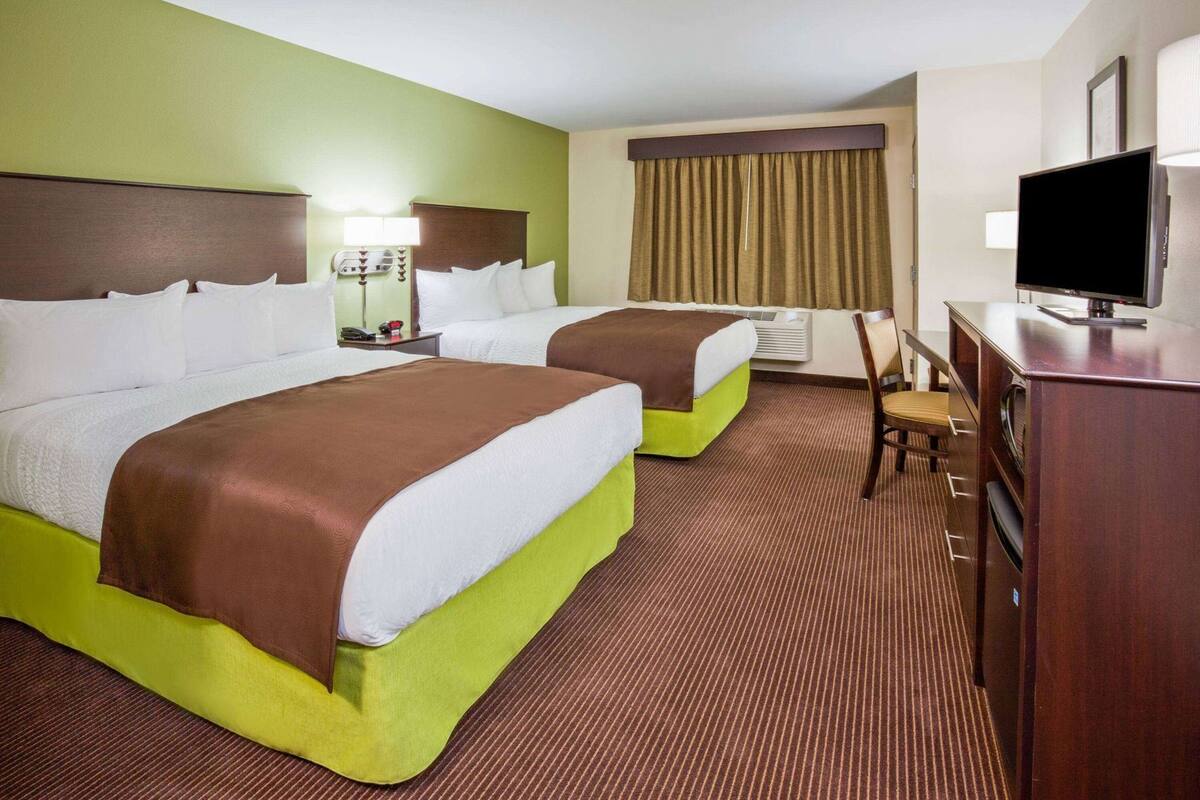 A hotel room with two beds, a desk, a television, and an air conditioning unit.