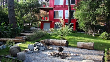 A red cabin with multiple windows, surrounded by a garden with rocks and a small tree.
